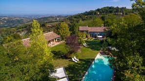 A villa with a swimming pool, surrounded by lush greenery and a view of the countryside.