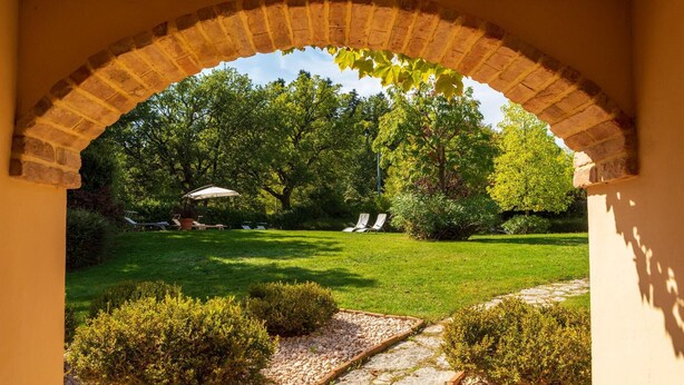 A garden with a brick archway, a lawn, and two lounge chairs under an umbrella. - La Tana del Ghiro 20 (Roncofreddo)