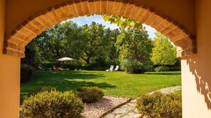 A garden with a brick archway, a lawn, and two lounge chairs under an umbrella. - La Tana del Ghiro 20 (Roncofreddo)