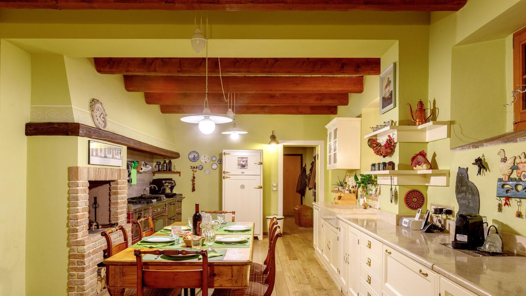 Un comedor acogedor con chimenea de ladrillo, vigas de madera en el techo y una cocina con armarios blancos y encimera.