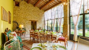 A dining area with a stone wall, wooden ceiling, and large windows. - La Tana del Ghiro 20 (Roncofreddo)