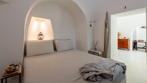 A minimalist bedroom with a large bed, a bedside table with a lamp, and a small table with a candle.