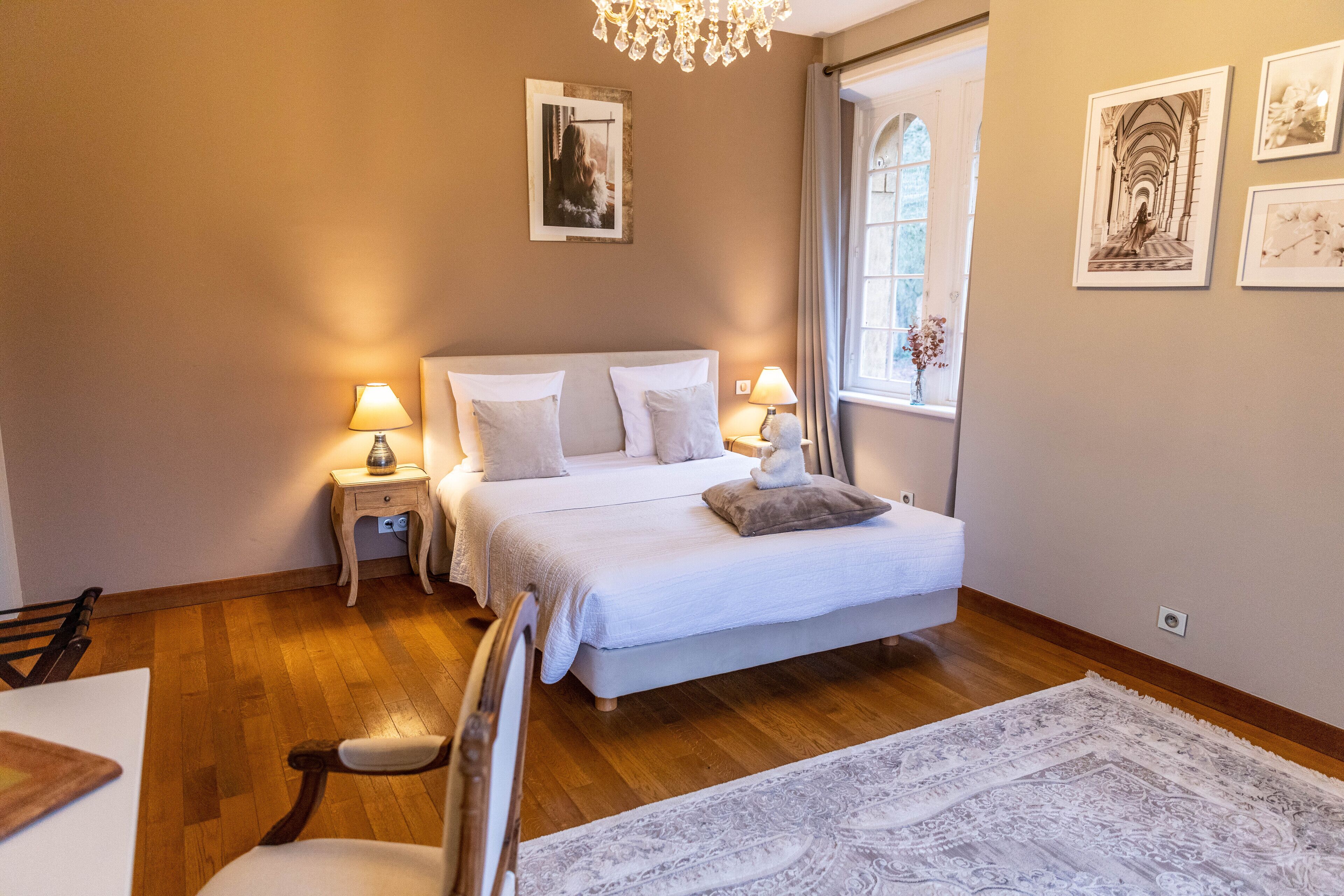 Un dormitorio con una cama grande, mesitas de noche con lámparas, un candelabro y cuadros enmarcados en las paredes.