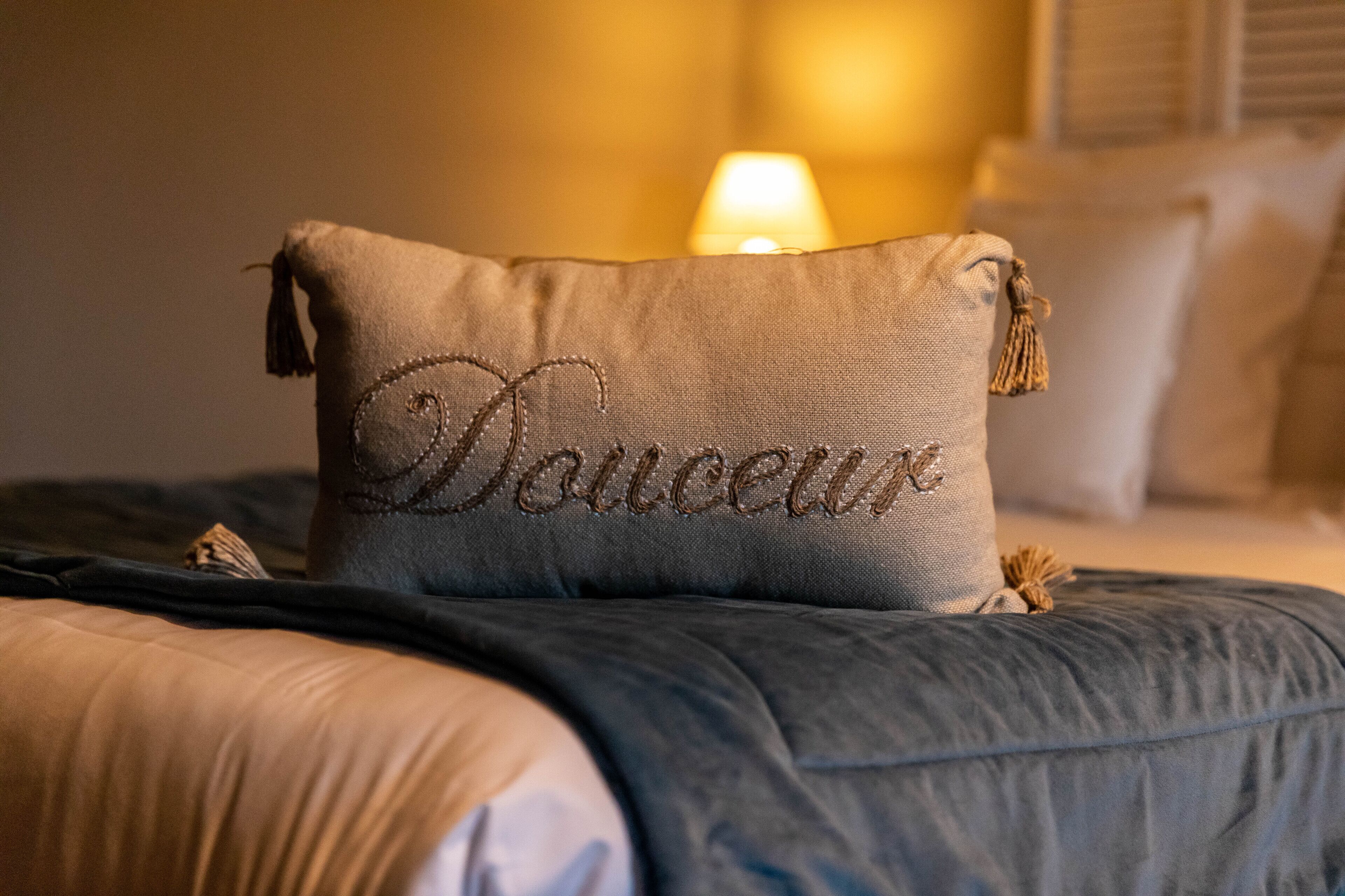 Una cama con un almohadón bordado con la palabra “Douceur” y flecos.