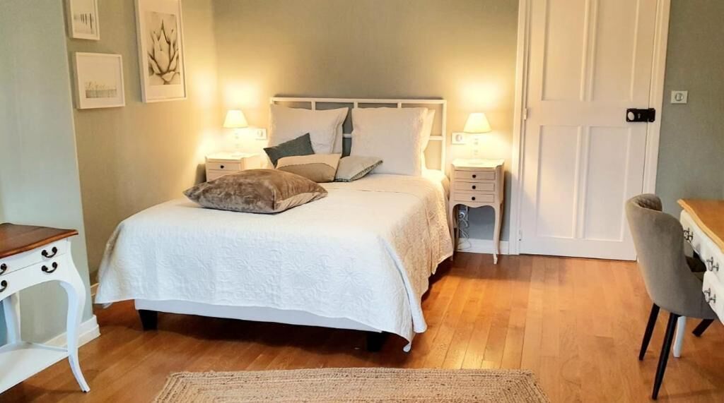Un dormitorio ordenado con cama, mesitas de noche, una silla y una puerta.