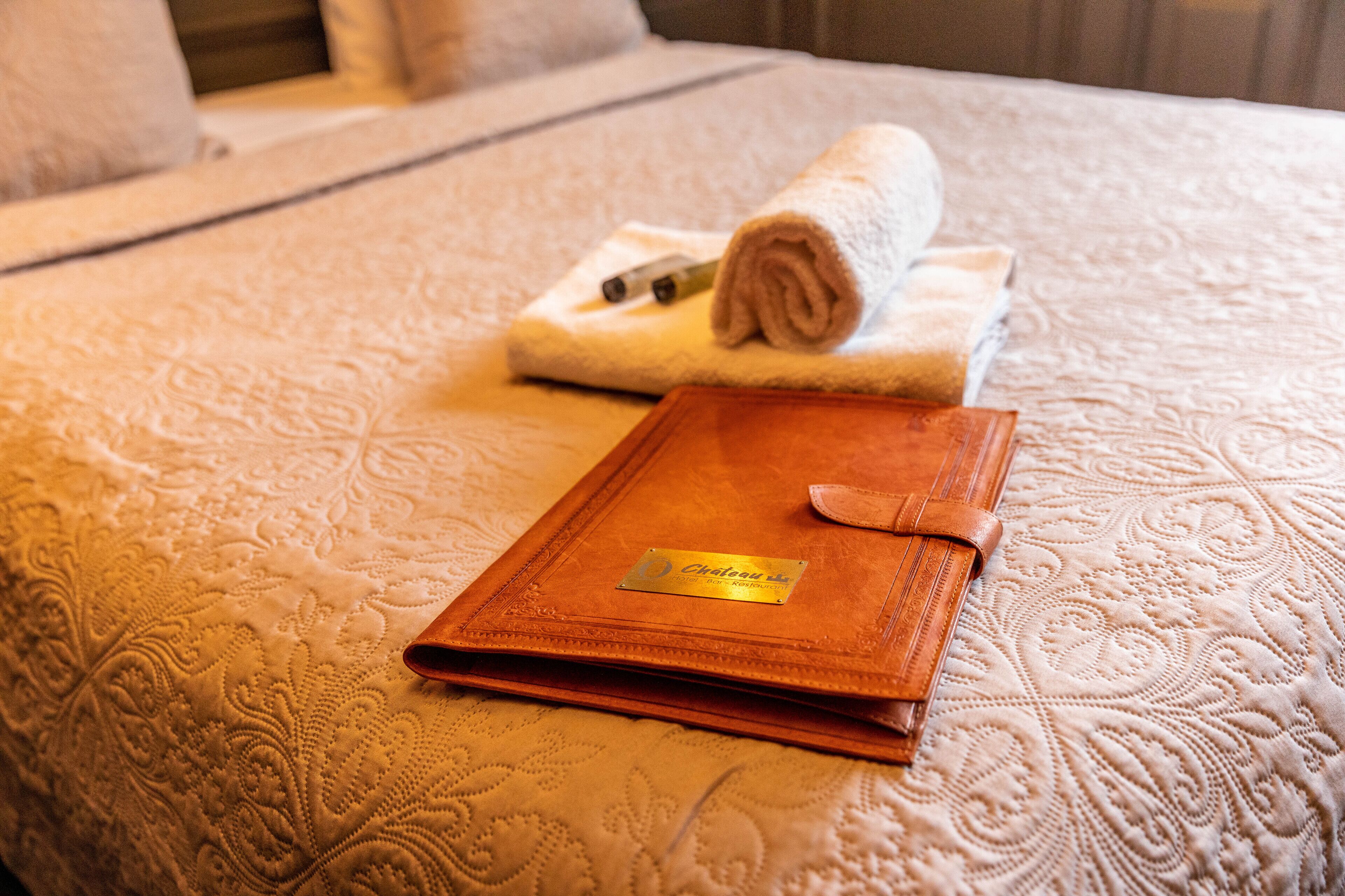 Una cama bien hecha con una toalla enrollada y un libro de tapa de cuero encima.