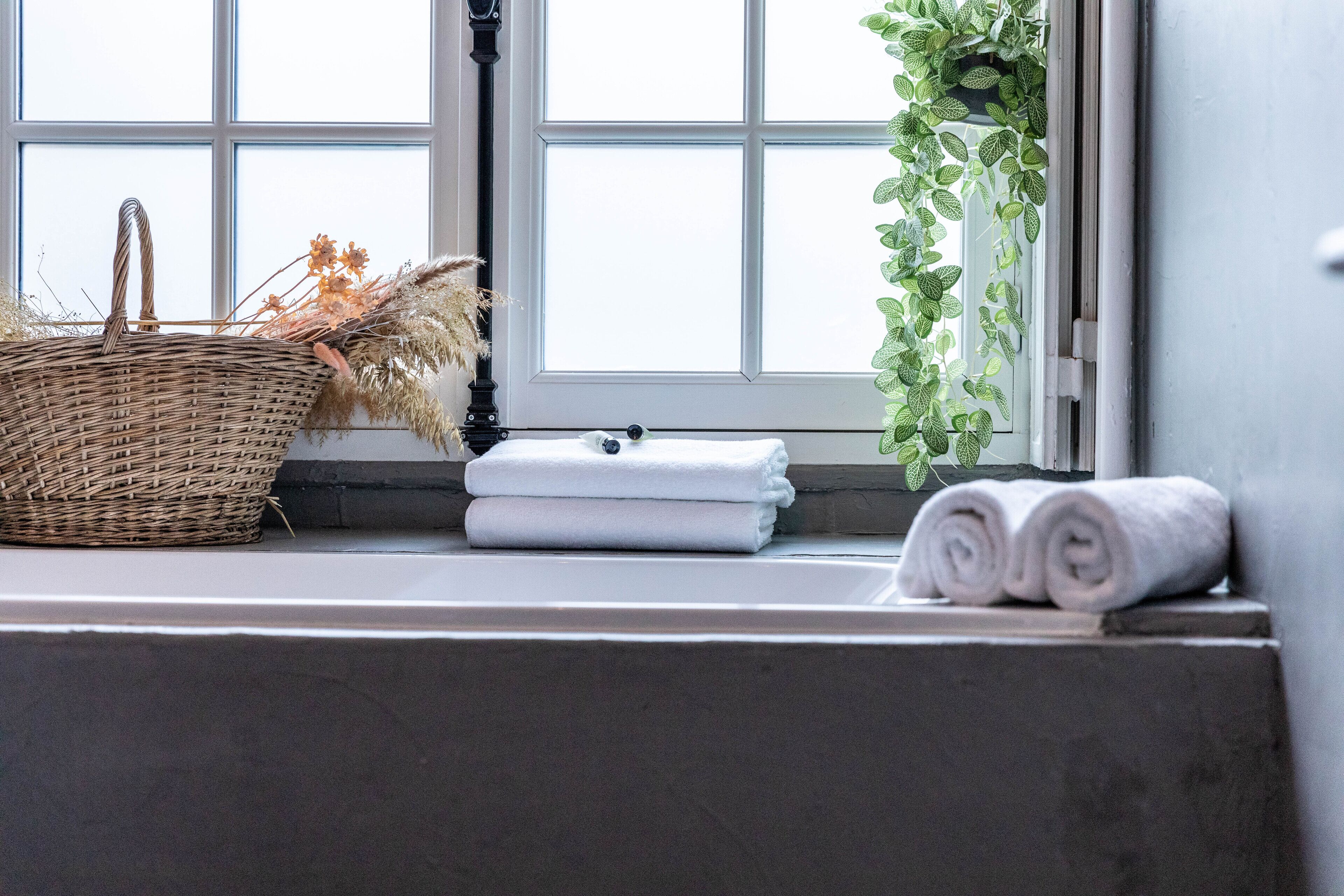 Ein Badezimmer mit einem Korbwäscher, gefalteten Handtüchern und einem Fenster mit Blick auf Grünflächen.