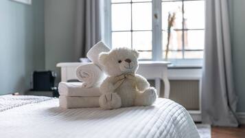 A bed with a white quilt, a white teddy bear, and rolled towels on it.