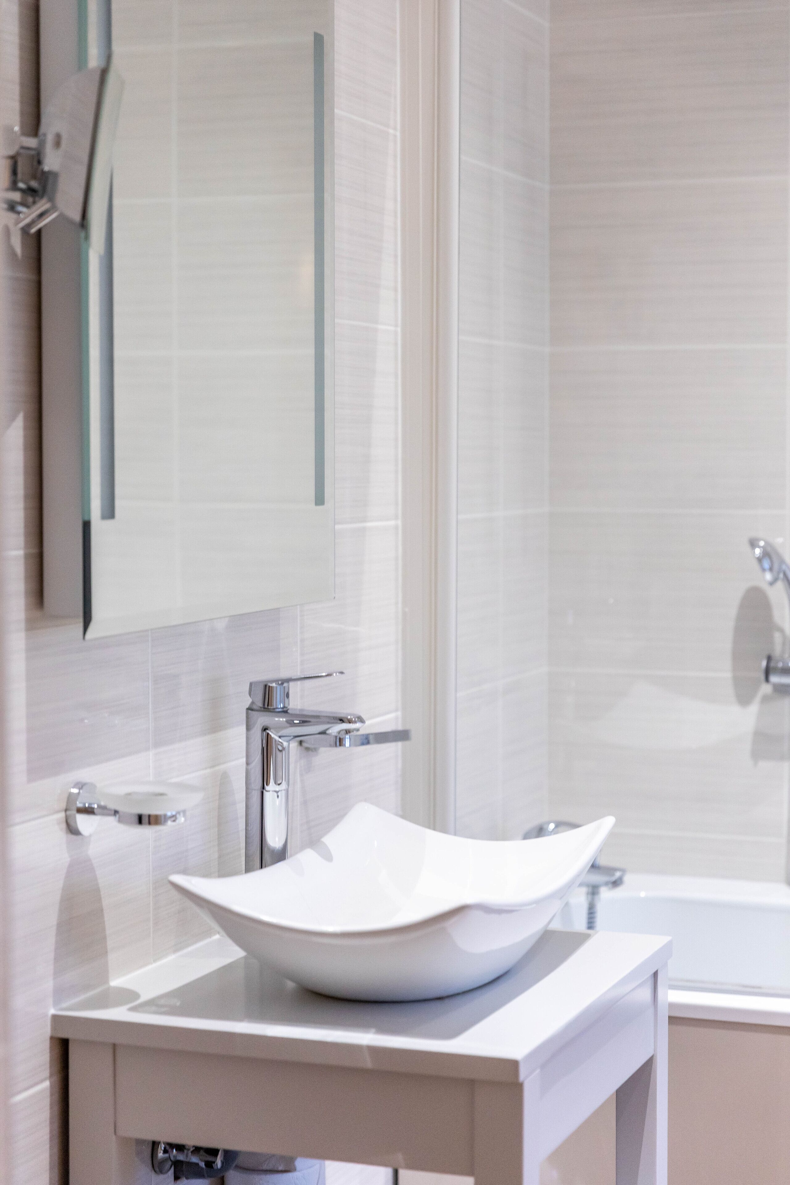 Ein modernes Badezimmer mit einem weißen Waschbecken, einem Spiegel und einer Badewanne.