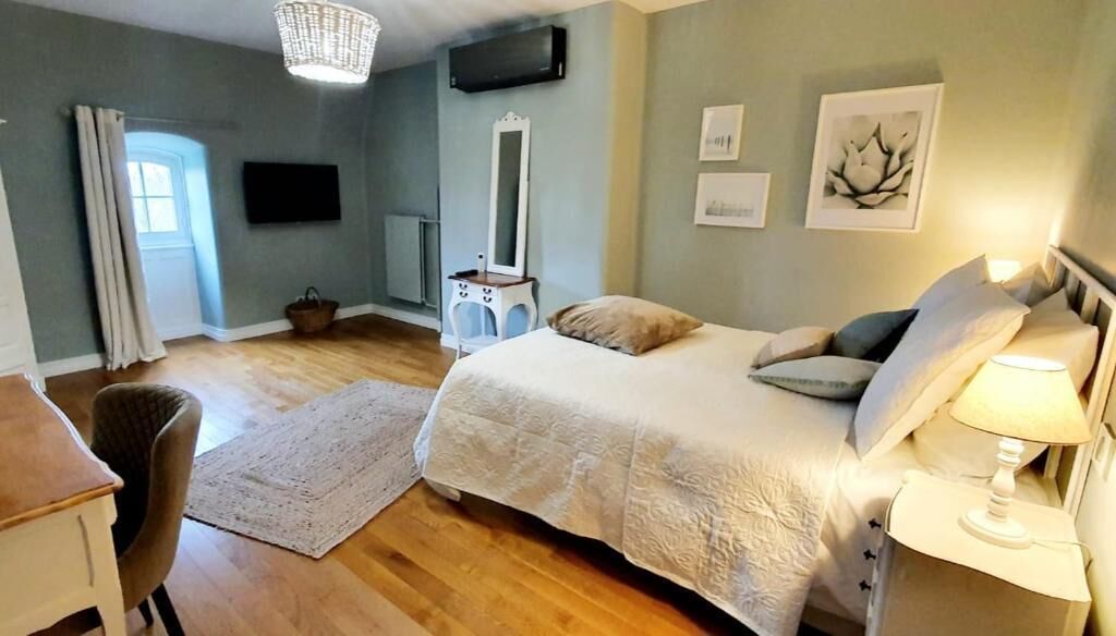Une chambre à coucher avec un lit, une table de chevet, une lampe et un miroir. On y trouve également une chaise et une petite table sur laquelle est posé un panier.
