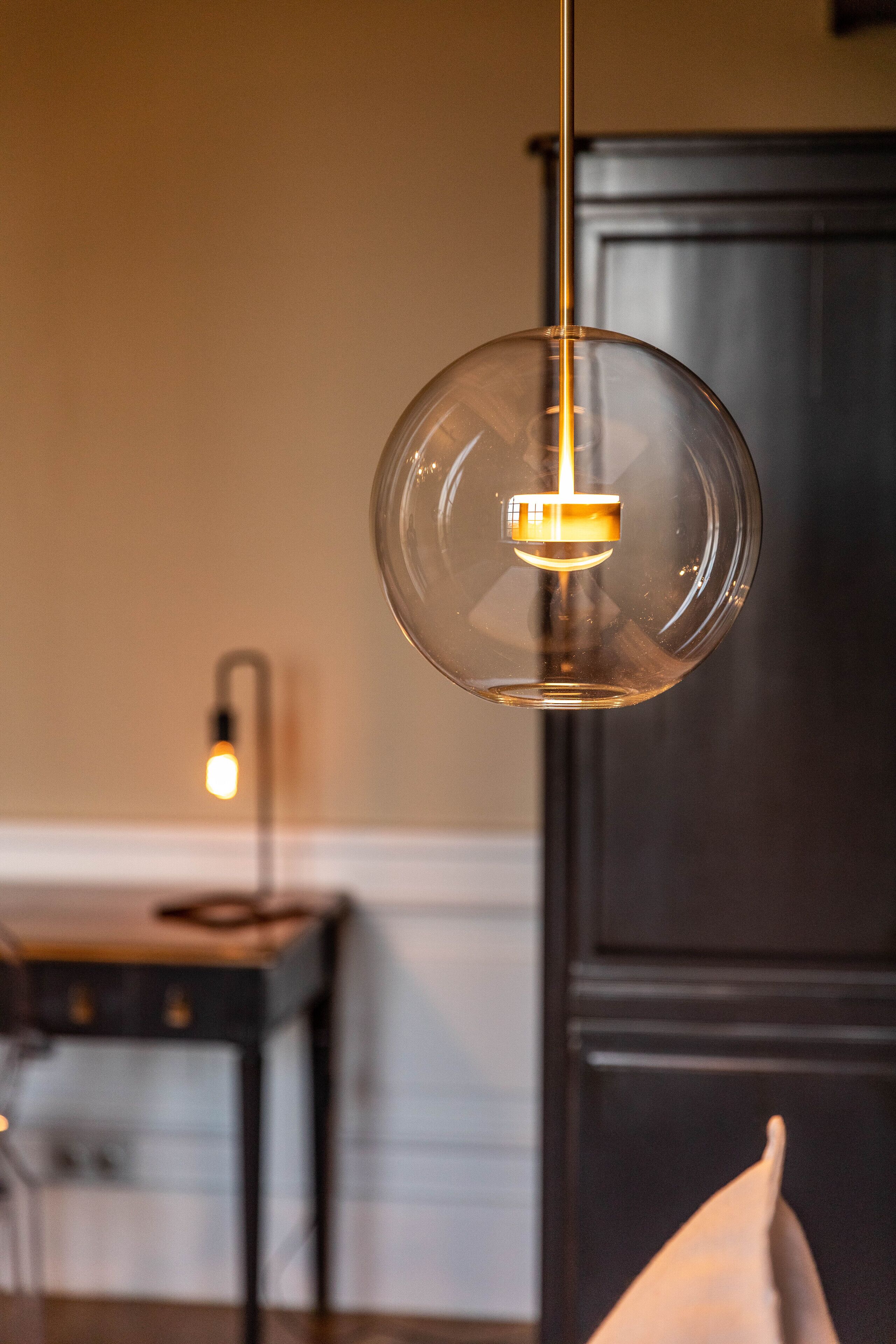 A modern interior with a clear glass pendant light, a dark wooden cabinet, and a white wall.