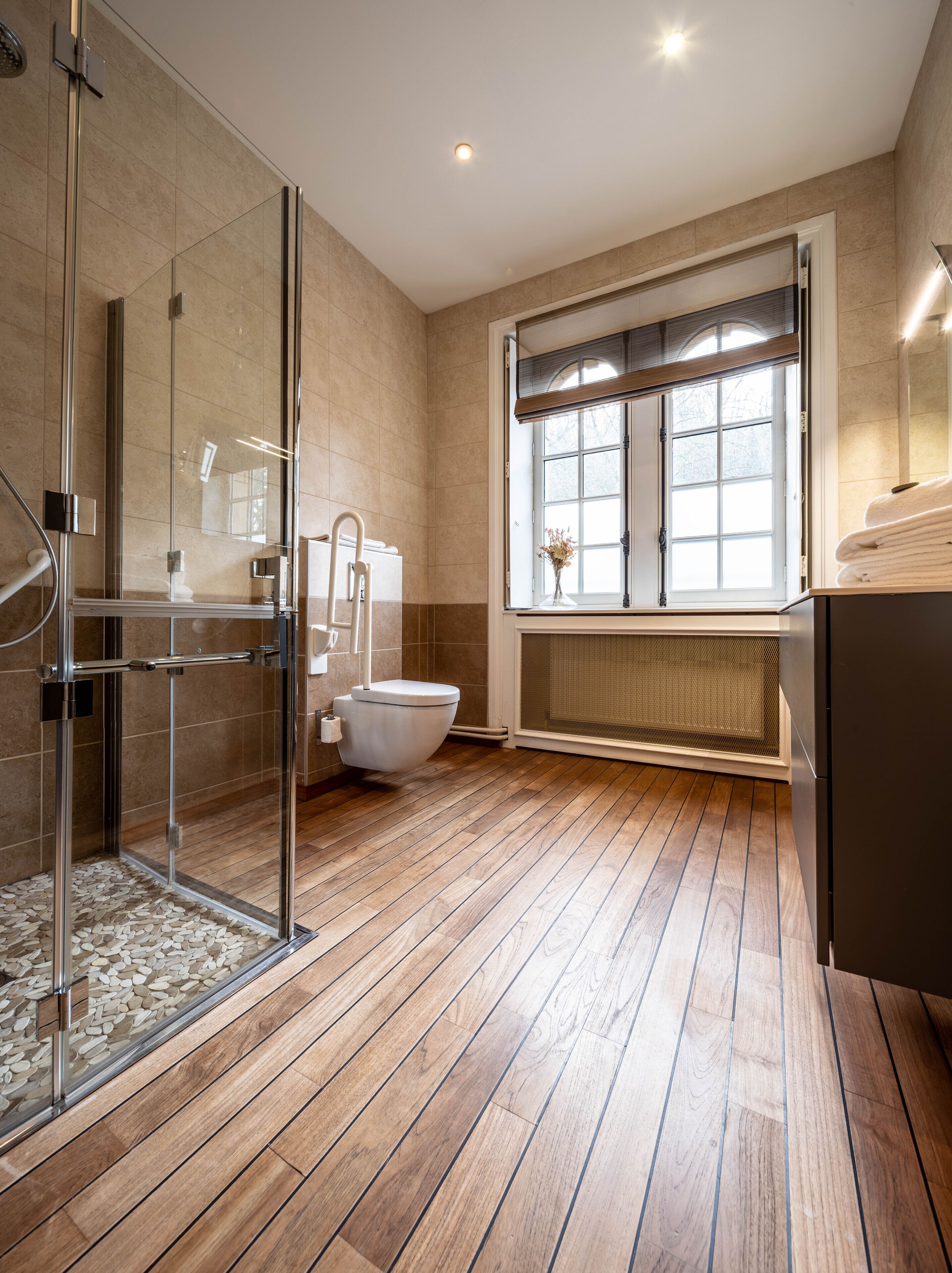 A modern bathroom with a glass shower enclosure, a white toilet, and a window with a view.