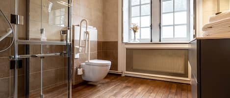 A modern bathroom with a glass shower enclosure, a white toilet, and a window with a view.