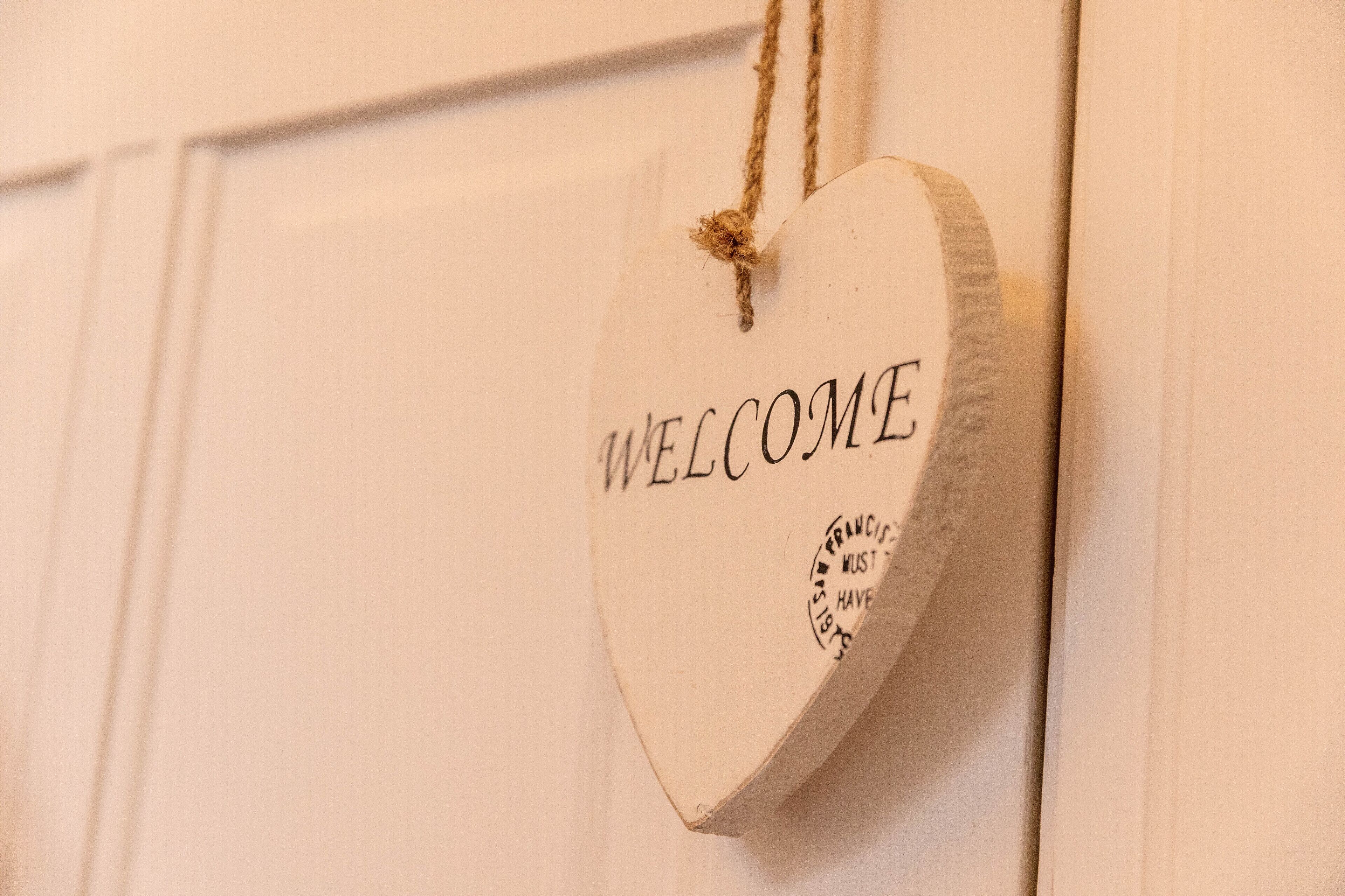 A heart-shaped welcome sign with the text "WELCOME" and a stamp that reads "SAN FRANCISCO MUST HAVE IT."