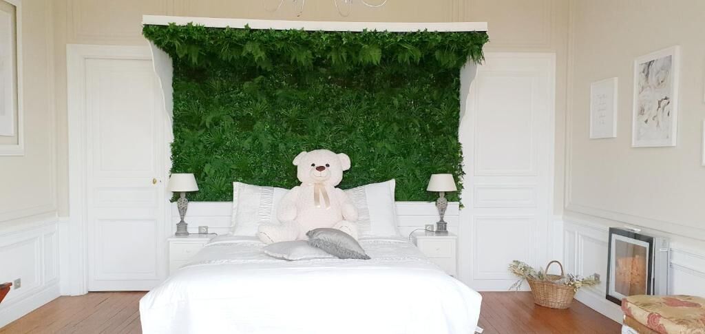 A bedroom with a bed, white walls, a green leafy wall, a white bear decoration, and a fireplace.