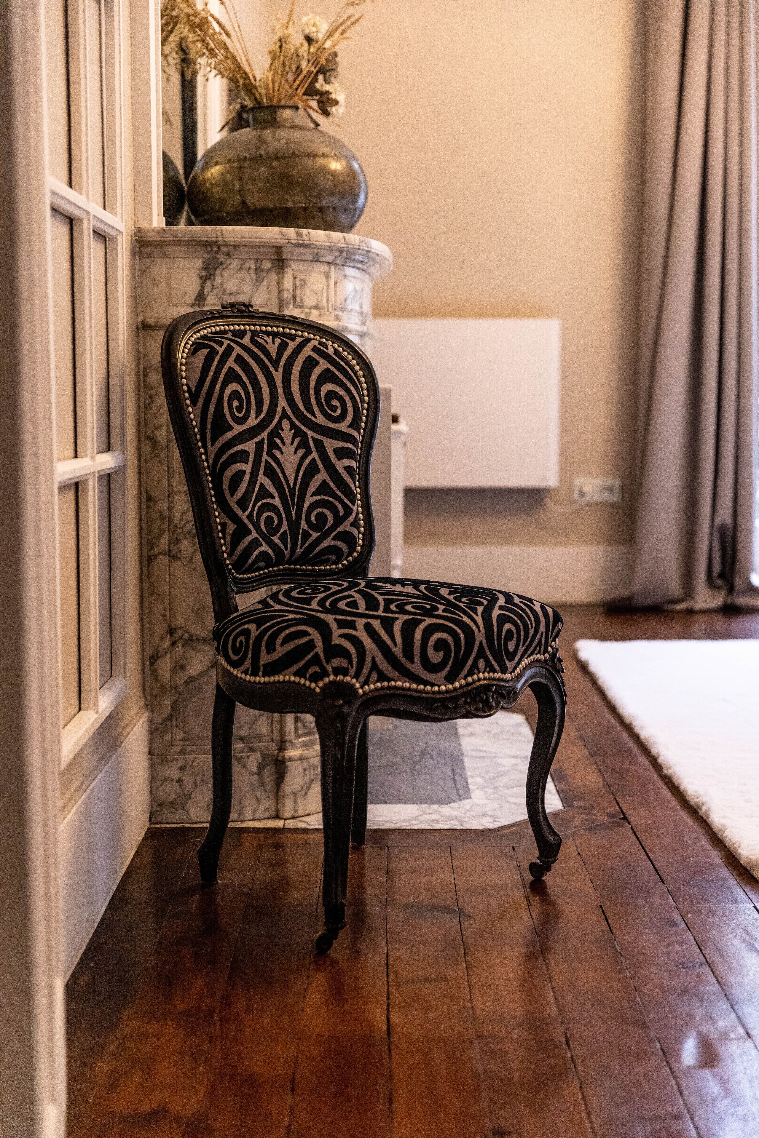 A chair with intricate black and white patterns, positioned in a room with a marble fireplace, wooden flooring, and a white wall unit.