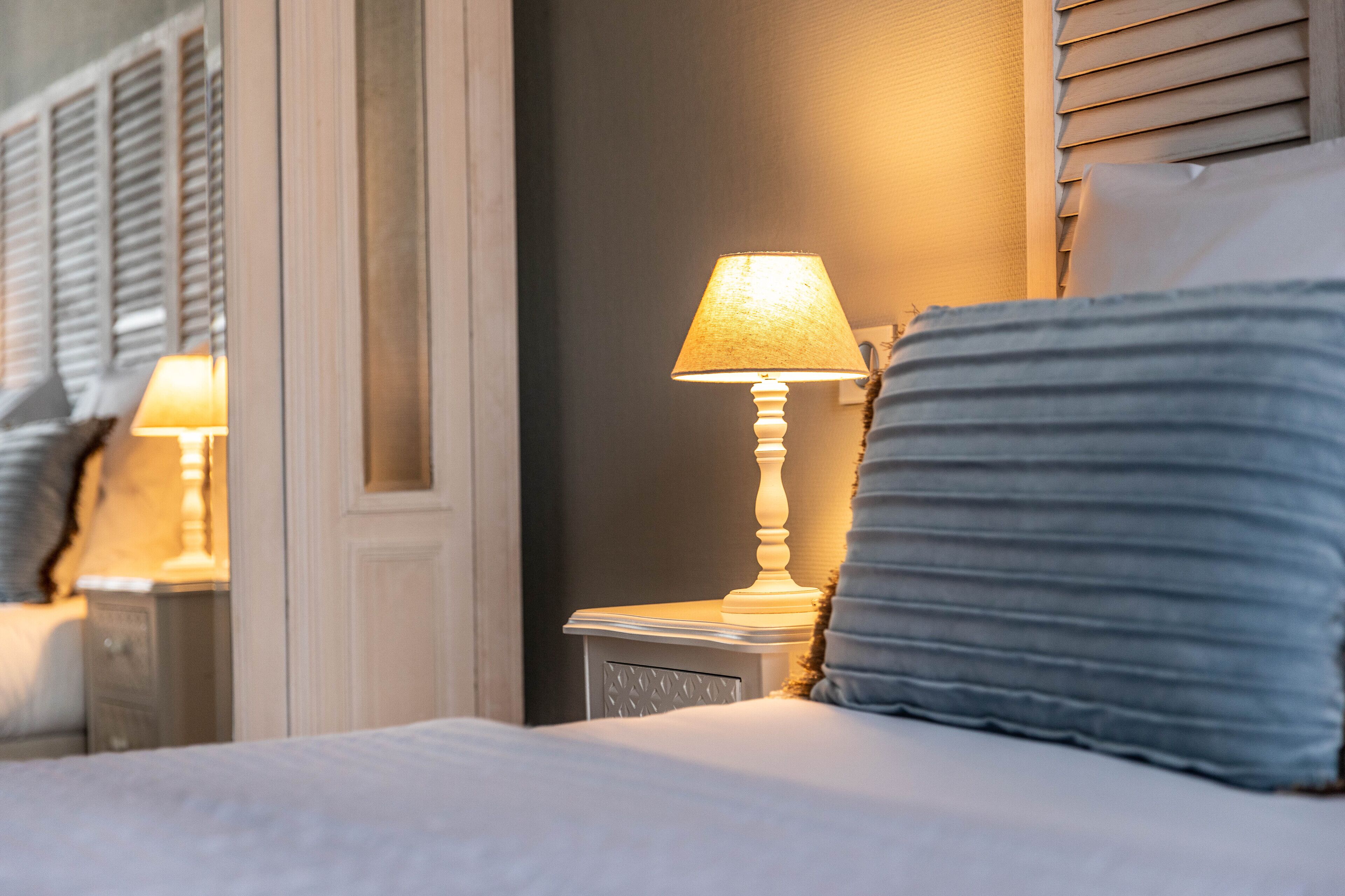A hotel room with a bed, a nightstand with a lamp, and a window with blinds.