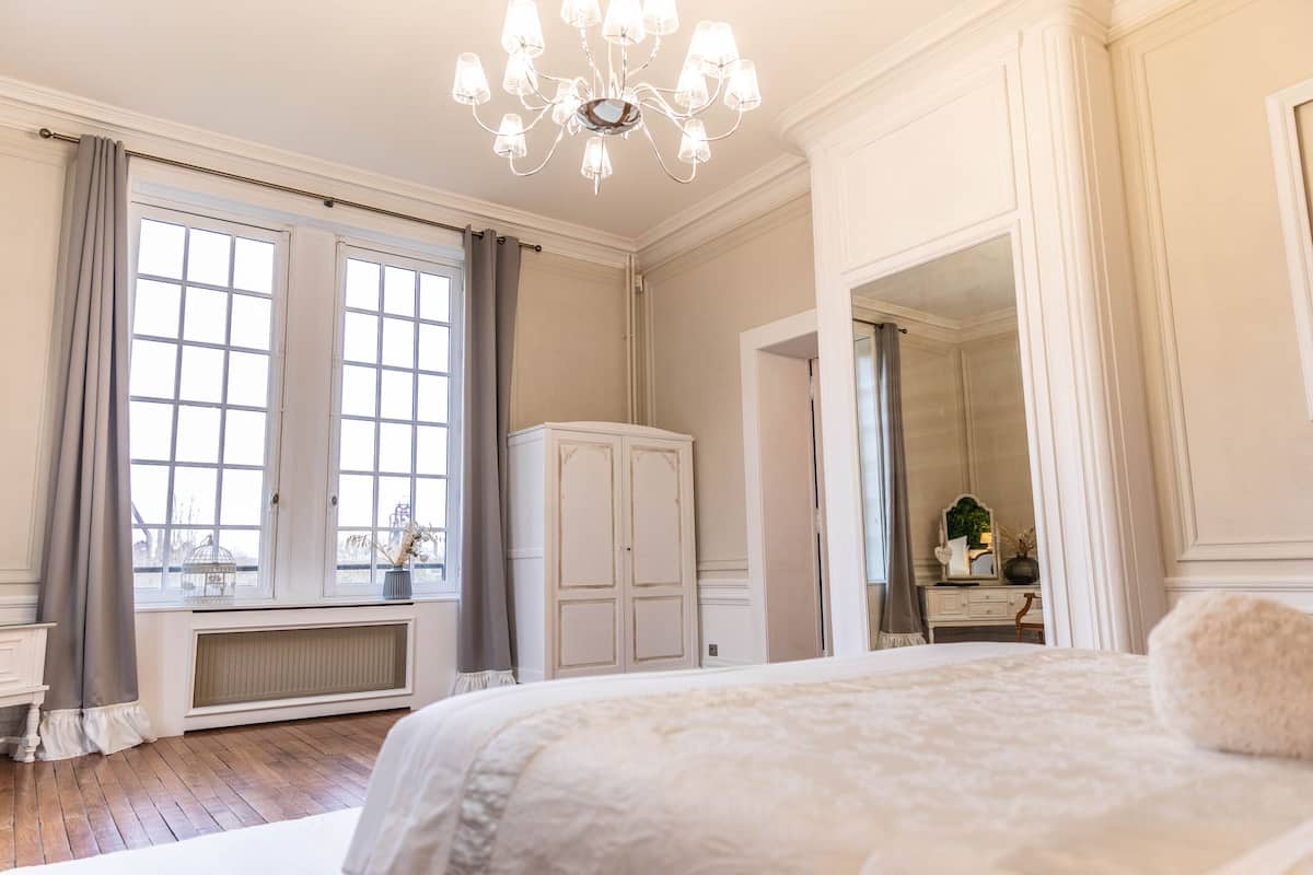 Un dormitorio con una cama grande, un aparador, un radiador y una ventana con cortinas.