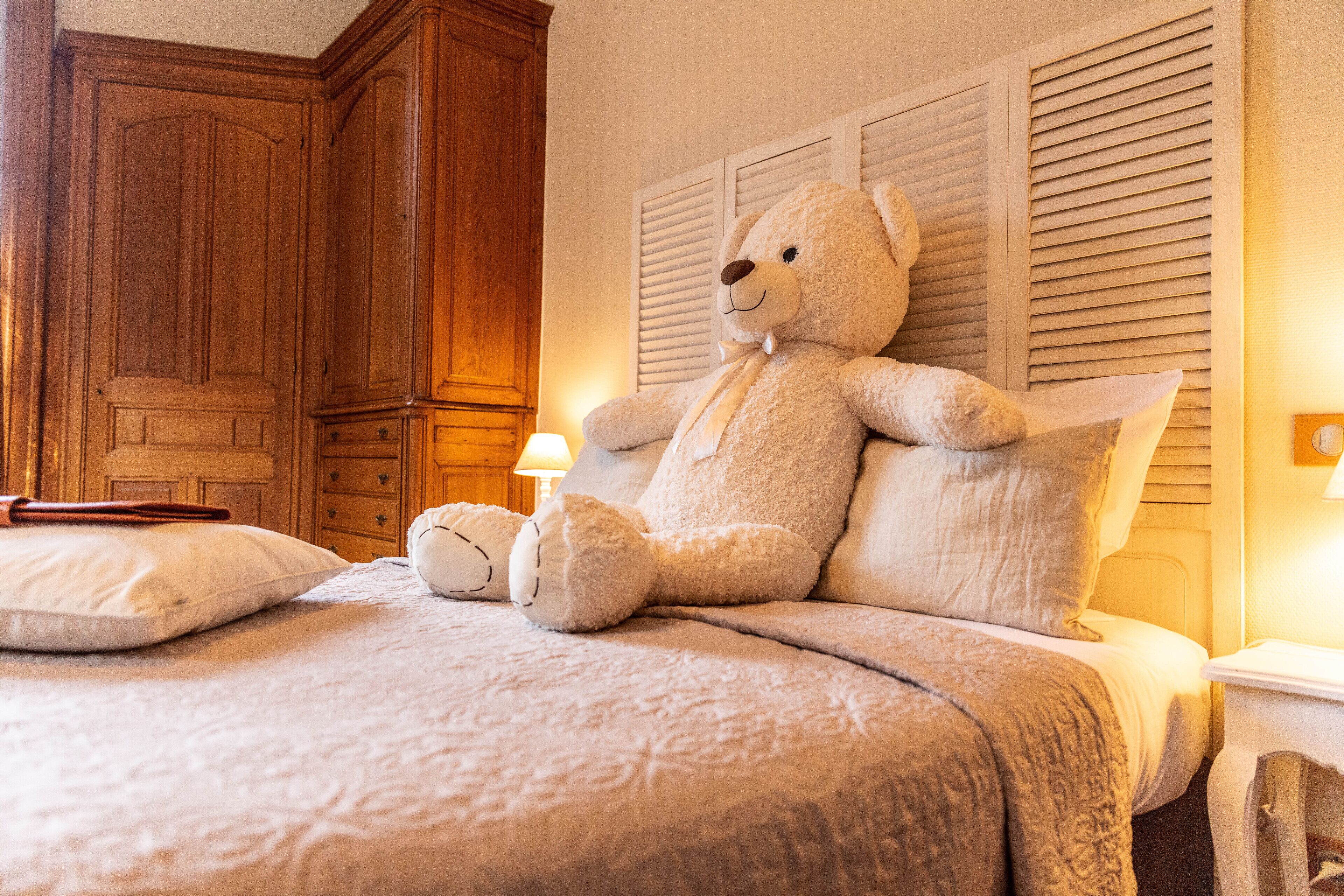 Une chambre à coucher avec un grand ours en peluche sur le lit, des meubles en bois et une lampe de chevet.