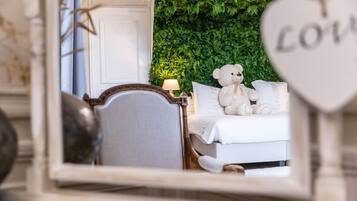 A bedroom with a bed, a teddy bear, a nightstand with a lamp, and a heart-shaped decoration with the word "LOVE".