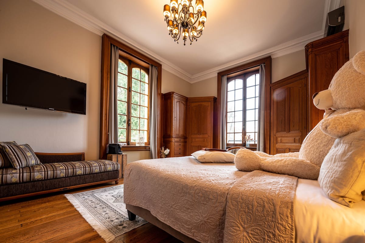 Un dormitorio espacioso con una cama grande, un sofá, suelo de madera y un candelabro.
