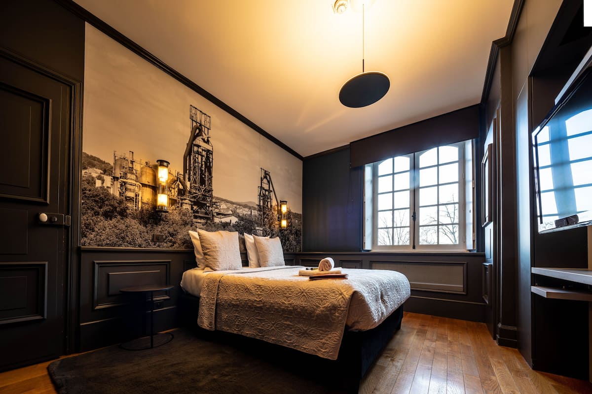 Un dormitorio con una cama grande, un tapete oscuro, un mural de paisaje urbano en la pared y una ventana con vistas.