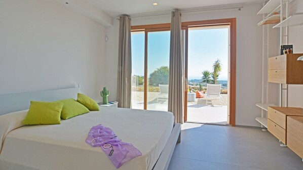 A bedroom with a bed, pillows, a nightstand, and a view of the outdoors through a sliding door.