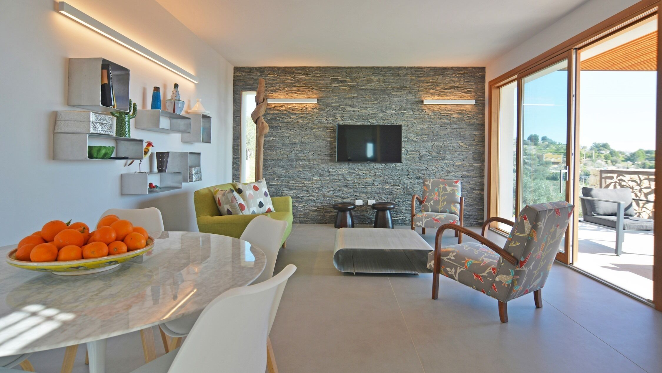 Un salon moderne avec un mur en pierre, un téléviseur à écran plat et un coin repas comprenant une table et des chaises.