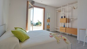 A bedroom with a bed, green pillows, a wooden dresser, a white chair, and a large window.