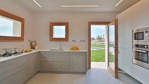 A modern kitchen with a built-in oven, a sink, and a window overlooking a garden. - Villa Gilda 5 1 in Avola (Avola)