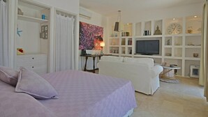 Ein Schlafzimmer mit einem Bett, einem weißen Sofa und einem Fernseher in einem Wohnbereich.