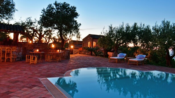 A poolside area with a stone patio, lounge chairs, and a bar area with candles. - Villa Passulunara 14 (Collesano)