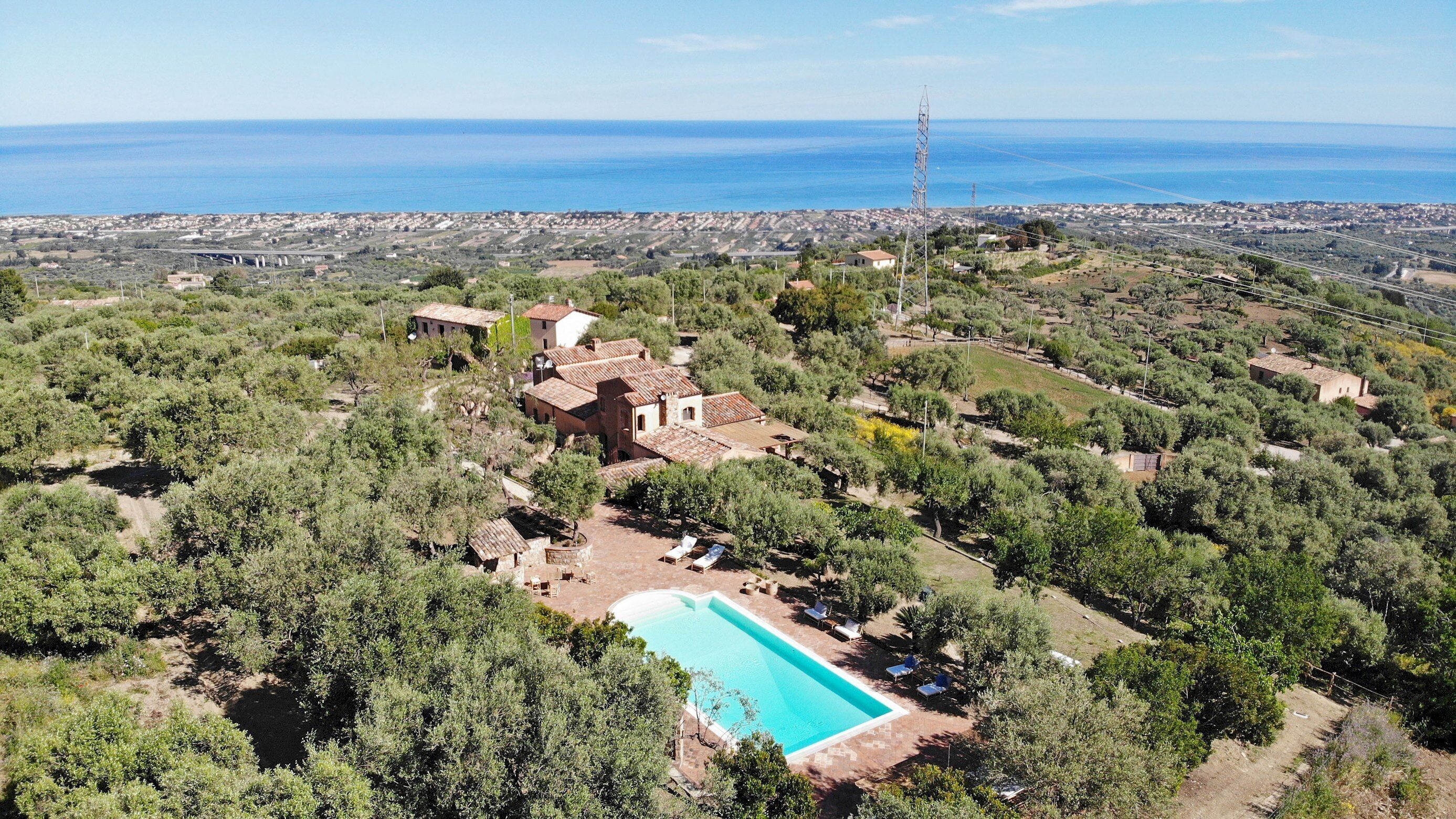 An aerial view of a property with a swimming pool, surrounded by trees and a view of the sea.