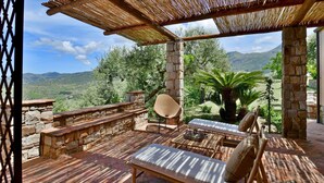 An outdoor patio with stone walls, wooden furniture, and a view of a mountainous landscape. - Villa Passulunara 14 (Collesano)