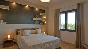 A bedroom with a large bed, bedside lamps, a built-in shelf with books, and a window with curtains. - Villa Provenza 12 4 in Cefal (Cefalù)