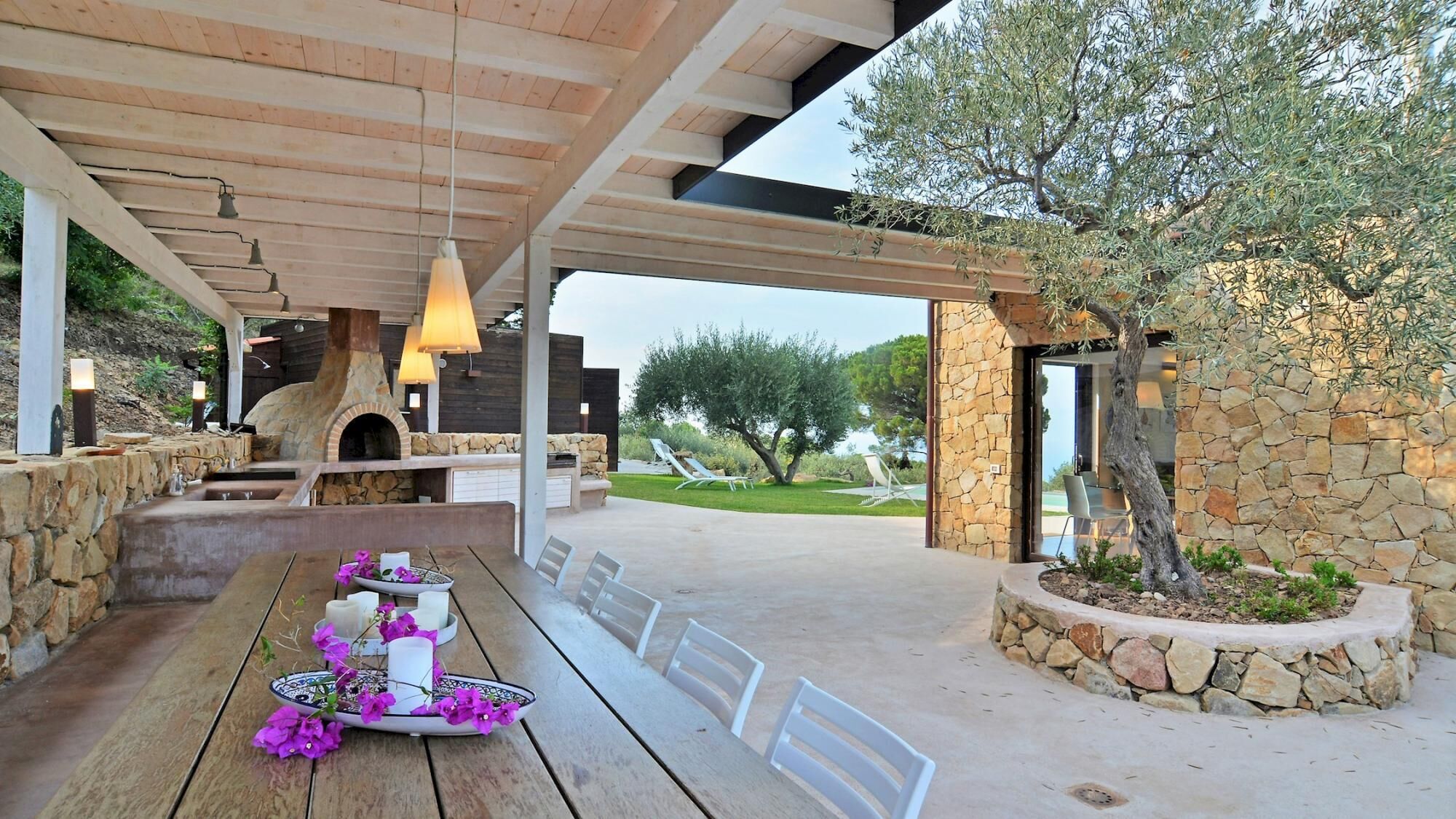 An outdoor dining area with a stone fireplace, wooden tables, and chairs.