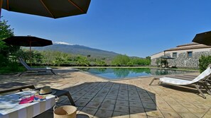 A pool area with lounge chairs and umbrellas, a table with items, and a mountain view in the background. - Villa Terre Normanne 13 (Castiglione di Sicilia)