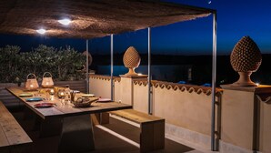 Een terras met eettable voor twee personen, omringd door een rieten dak en uitzicht op de nachthemel.