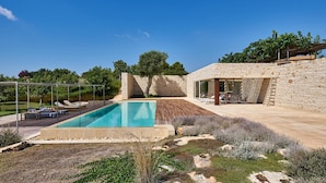 A modern outdoor pool area with a stone wall, lounge chairs, and a pergola. - Villa Majoli 9 in Noto (Noto)
