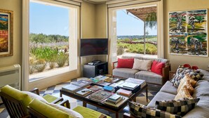 A living room with a large window, a flat-screen TV, a sofa, a coffee table with books, and a painting on the wall. - Villa Majoli 9 in Noto (Noto)