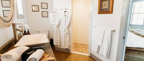 Un baño moderno con lavabo, espejo y toallero. Se observan dos albornoces blancos colgados en la pared.