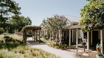 A covered outdoor seating area with tables and chairs, surrounded by a gravel path and various plants.