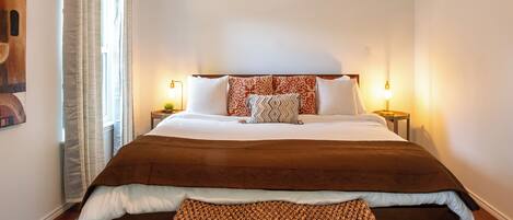 A neatly made bed with a brown blanket, a patterned pillow, and a matching bench.