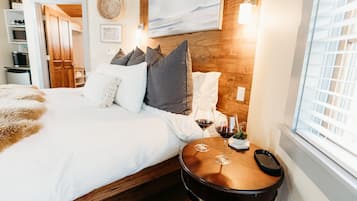 A neatly made bed with white and gray bedding, a wooden headboard, and two bedside tables with wine glasses.