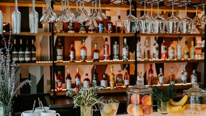 Een bar met flessen drank, hangende wijnglazen en diverse baraccessoires en ingrediënten op de toonbank.
