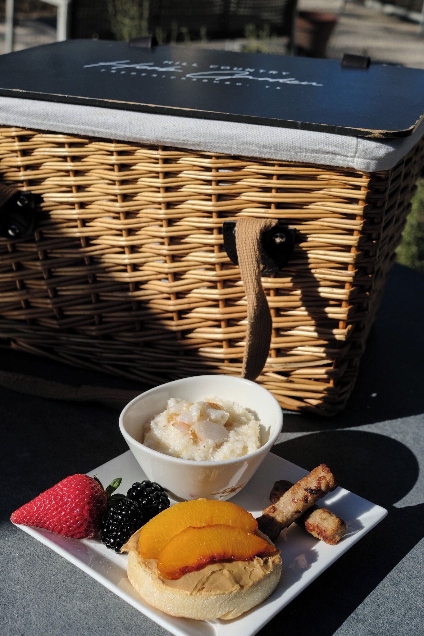 A wicker picnic basket with a handle, a white plate with a dessert, and a bowl of ice cream.