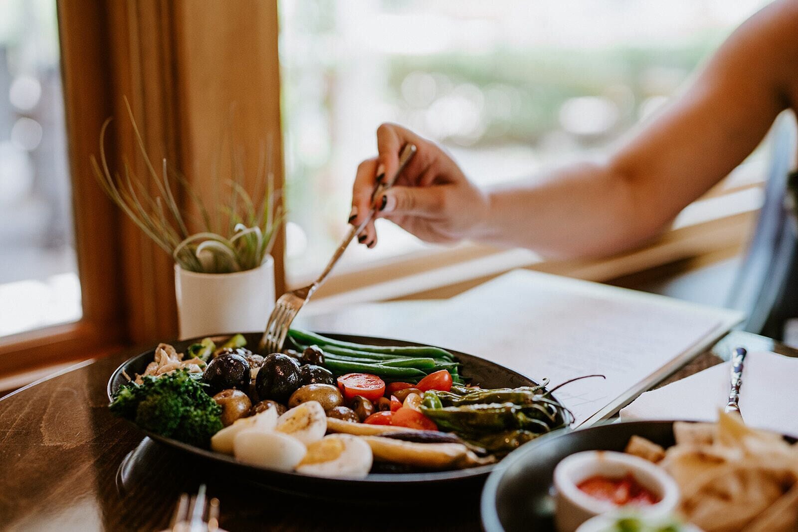 A person dining at a table with a variety of vegetables and a small bowl of sauce.