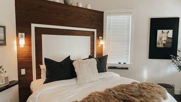 Quarto com cabeceira de madeira, roupa de cama branca, um cobertor marrom fofinho e um ventilador de teto.