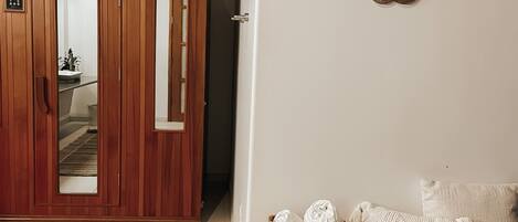 A room with a wooden wardrobe, a bench with cushions, and a decorative wall piece.
