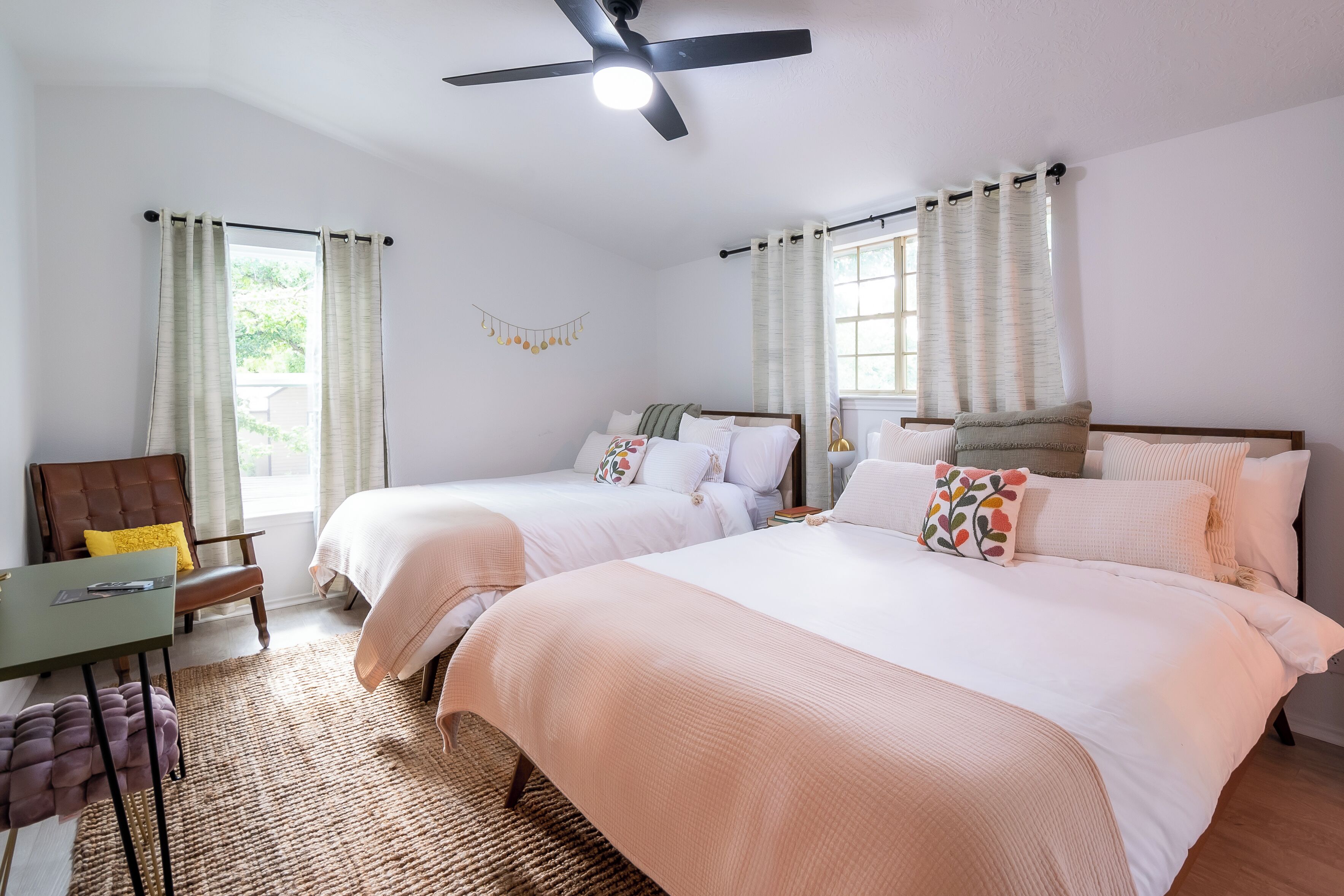 A hotel room with two beds, a desk, a chair, and a ceiling fan.